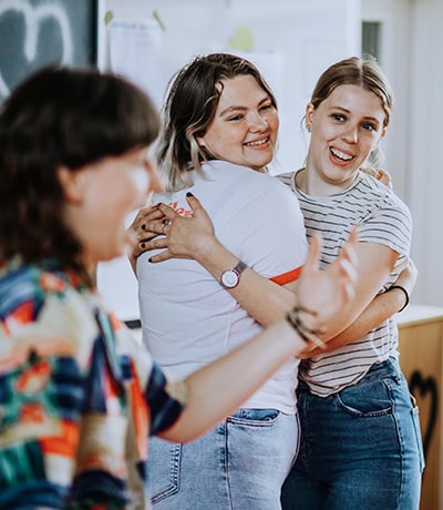 Vrouw en meisje lachend en knuffelend op school, inclusief leraar op achtergrond, in klaslokaalomgeving, vrolijke sfeer, vriendschap, educatie, bonding, positieve interactie, scholing, schoolactiviteiten, welzijn, educatieve setting.